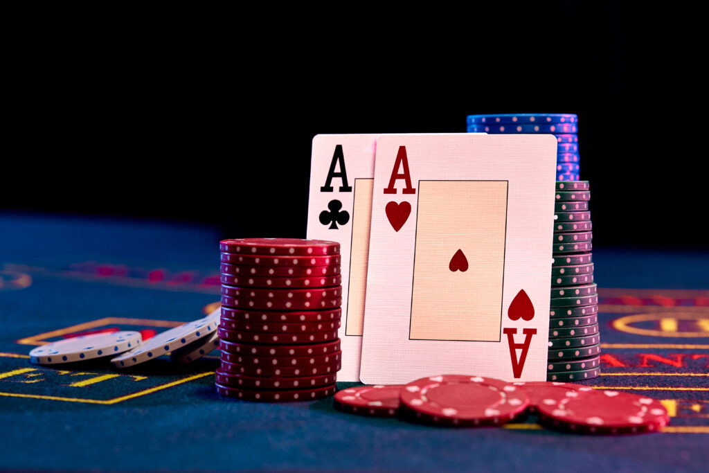 Two aces standing leaning on chips piles, some of them are laying nearby on blue cover of playing table. Black background. Casino concept. Close-up.