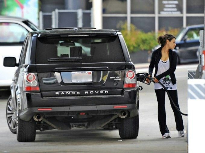 Mila kunis, dressed informally, filling gas in her range rover at a gas station.